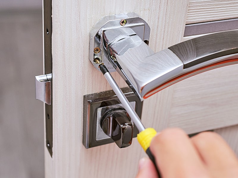 Fotografía de una puerta con un pomo siendo desatornillado con un destornillador.