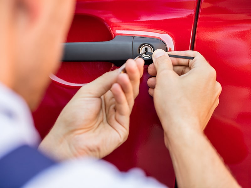 Fotografía de un cerrajero abriendo la puerta de un coche rojo con una ganzua.